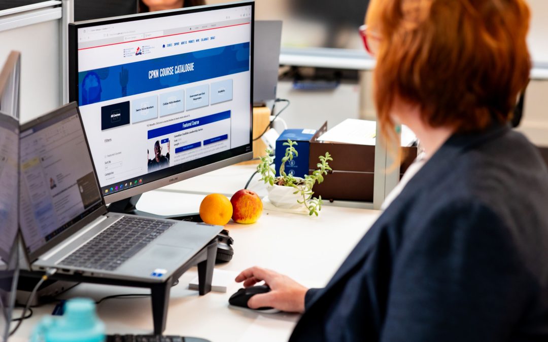 Woman sitting at her desk in an office, looking at a computer screen showing CPKN course catalogue webpage.