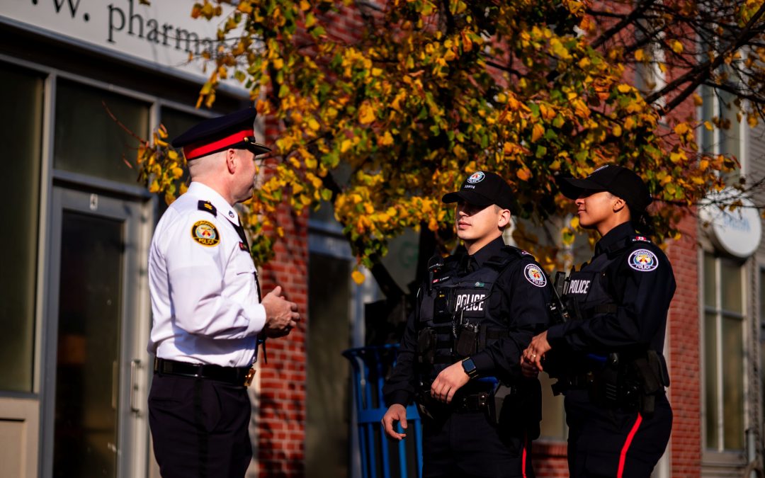 A senior officer in a white shirt talks to two Toronto Police Service cadets in uniform.