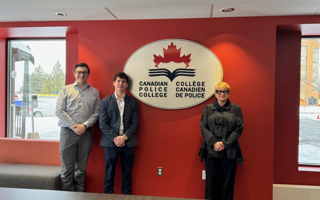 Two men and a woman standing in front of a red wall with a logo sign for the Canadian Police College.