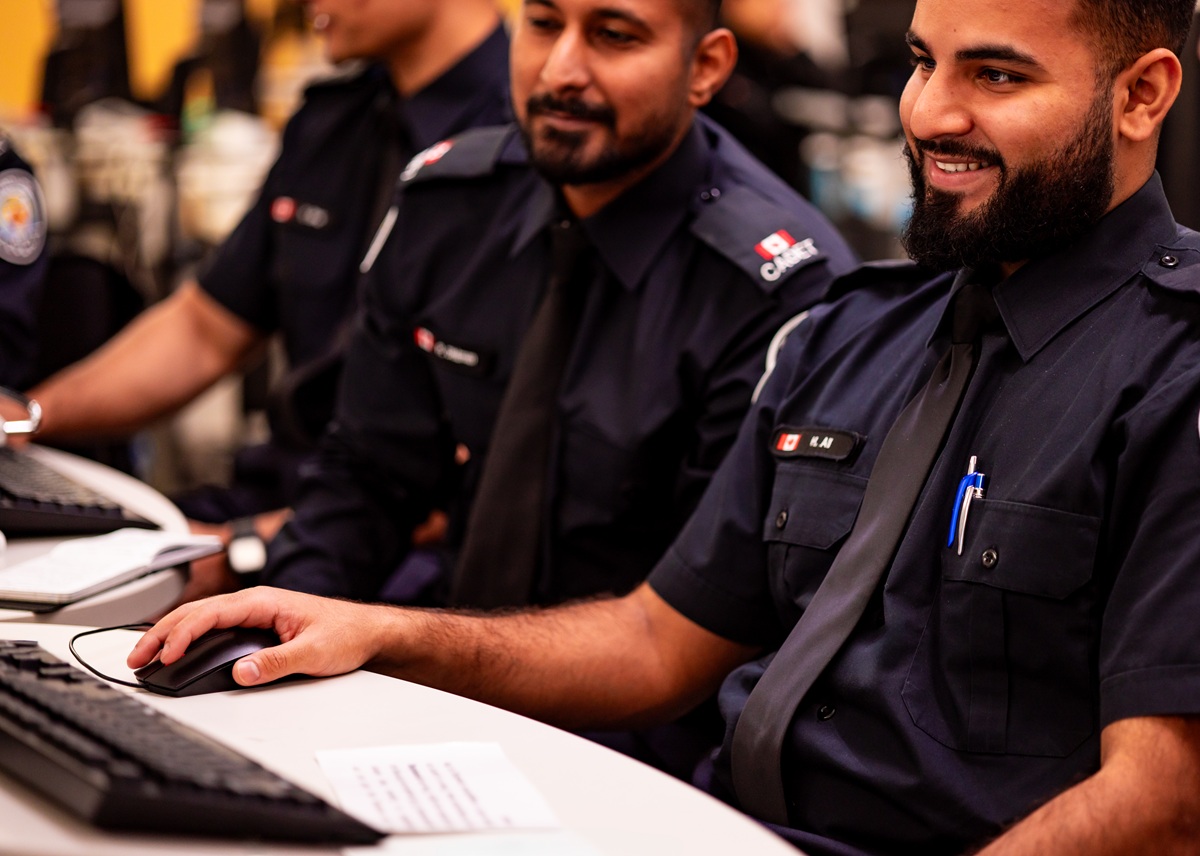 Deux cadets de police regardent un ordinateur. L’un d’eux a la main droite sur une souris et sourit. L’autre regarde l’écran.