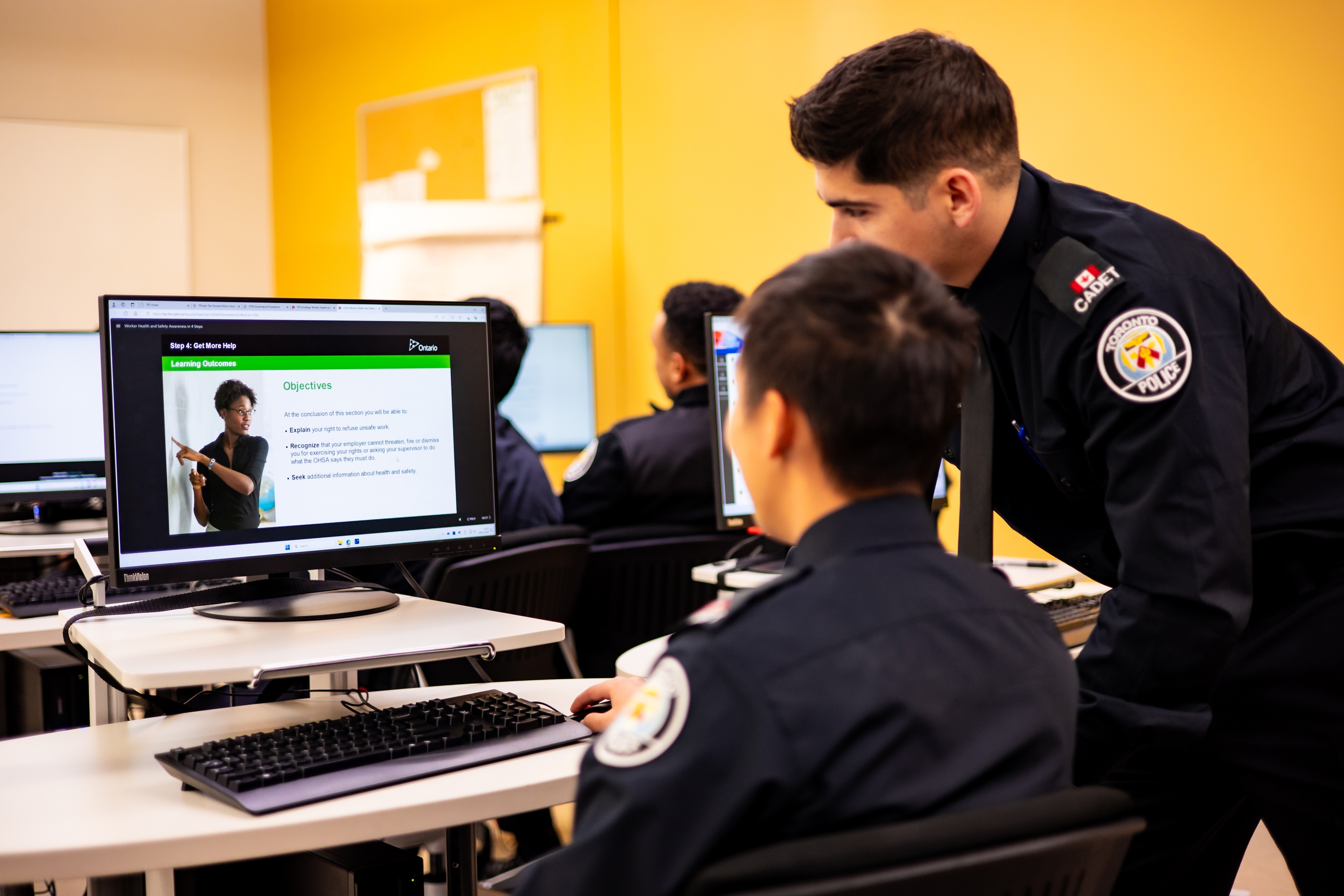 Two uniformed police cadets looking at a computer screen, showing an e-learning course.